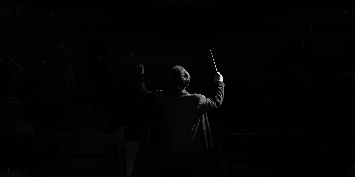 Un direttore d'orchestra dirige un'orchestra con una bacchetta tenuta alta.