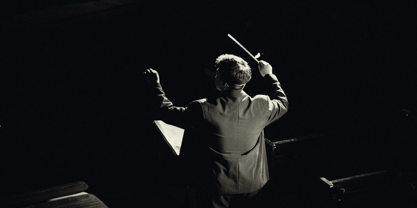 Direttore d'orchestra che alza la bacchetta su un palco buio.